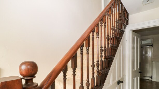 A wooden staircase with a rounded baluster and a white door at the bottom. - The Vale (Beaworthy)