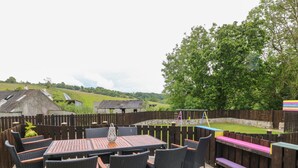 An outdoor patio with a table and chairs, a swing set, and a view of a rural landscape. - The Vale (Beaworthy)
