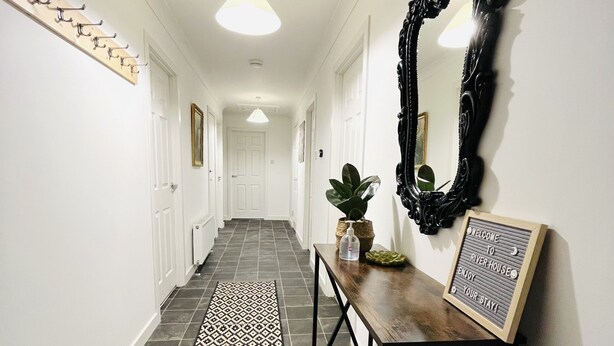 Un couloir avec un tapis à motifs, une console en bois, un miroir et une pancarte de bienvenue.