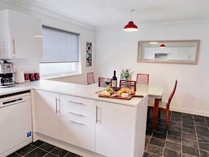 A modern kitchen with white cabinets, a dining area with a table and chairs, and a red pendant light. - Peaceful bungalow, super close to birnam oak and hiking trails. (Dunkeld)