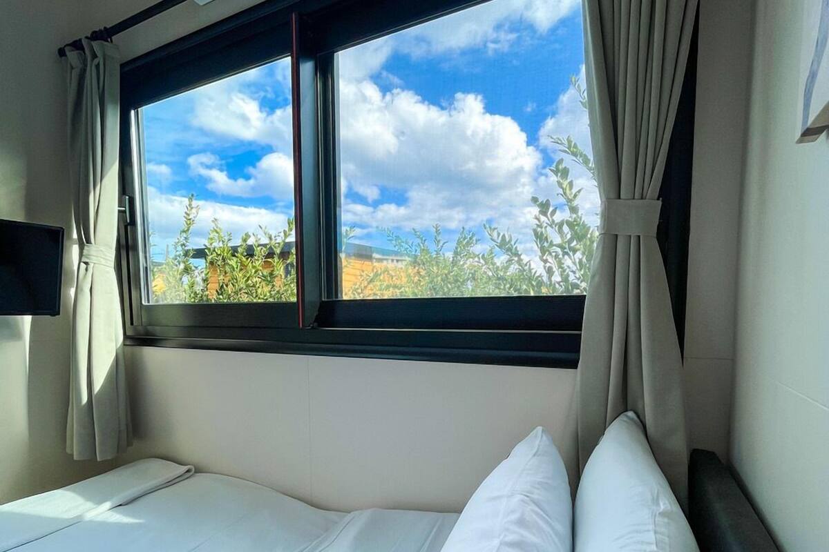 Una habitación de hotel con cama, ventana con cortinas y un equipo de aire acondicionado.