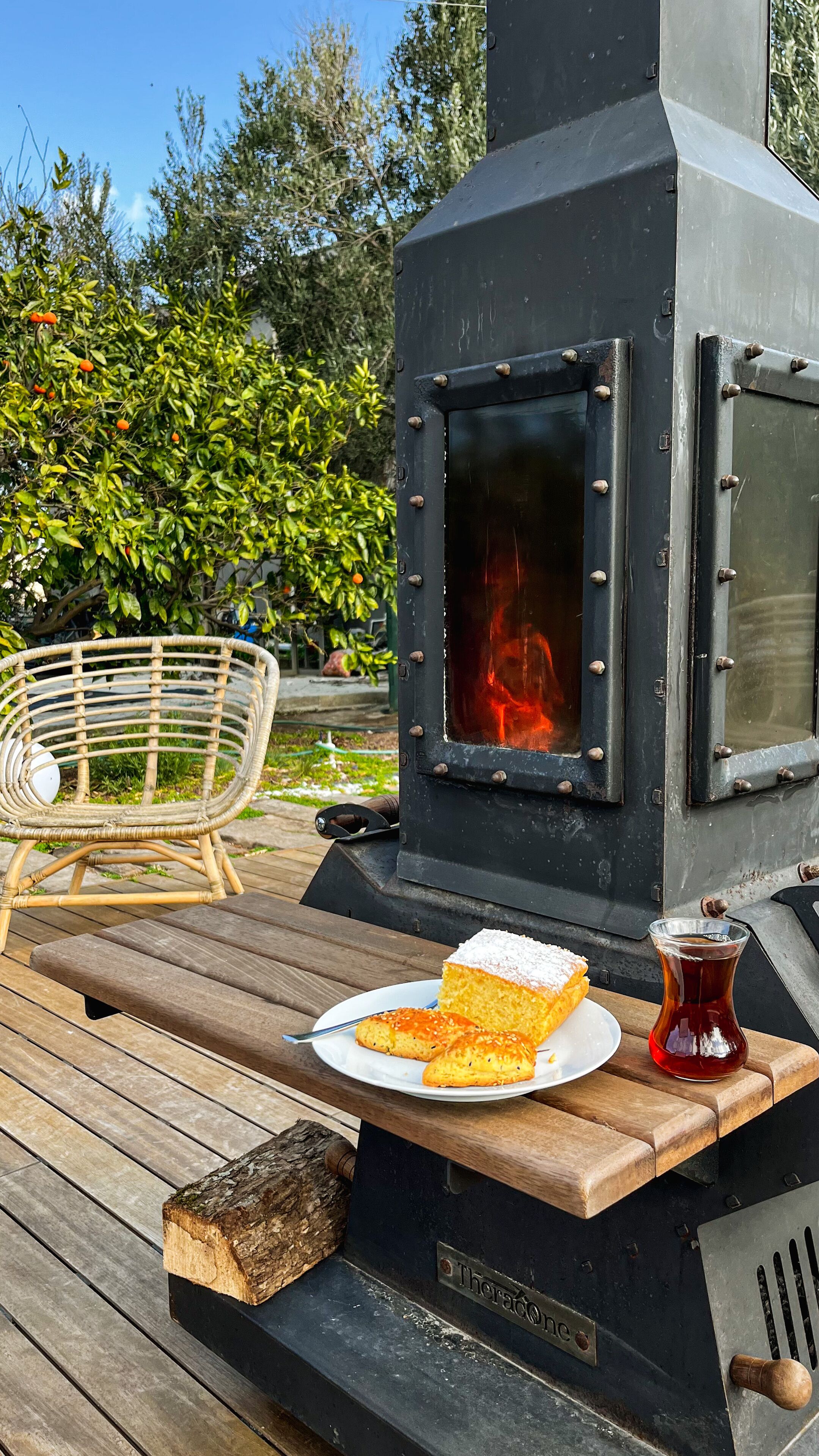 A wood-burning stove with a plate of food and a drink on a wooden deck.