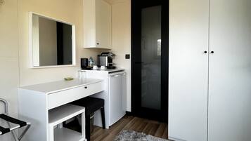 Et moderne, minimalistisk soveværelse med et hvidt skab, et skrivebord med stol, et lille køleskab og en blød måtte på trægulvet.