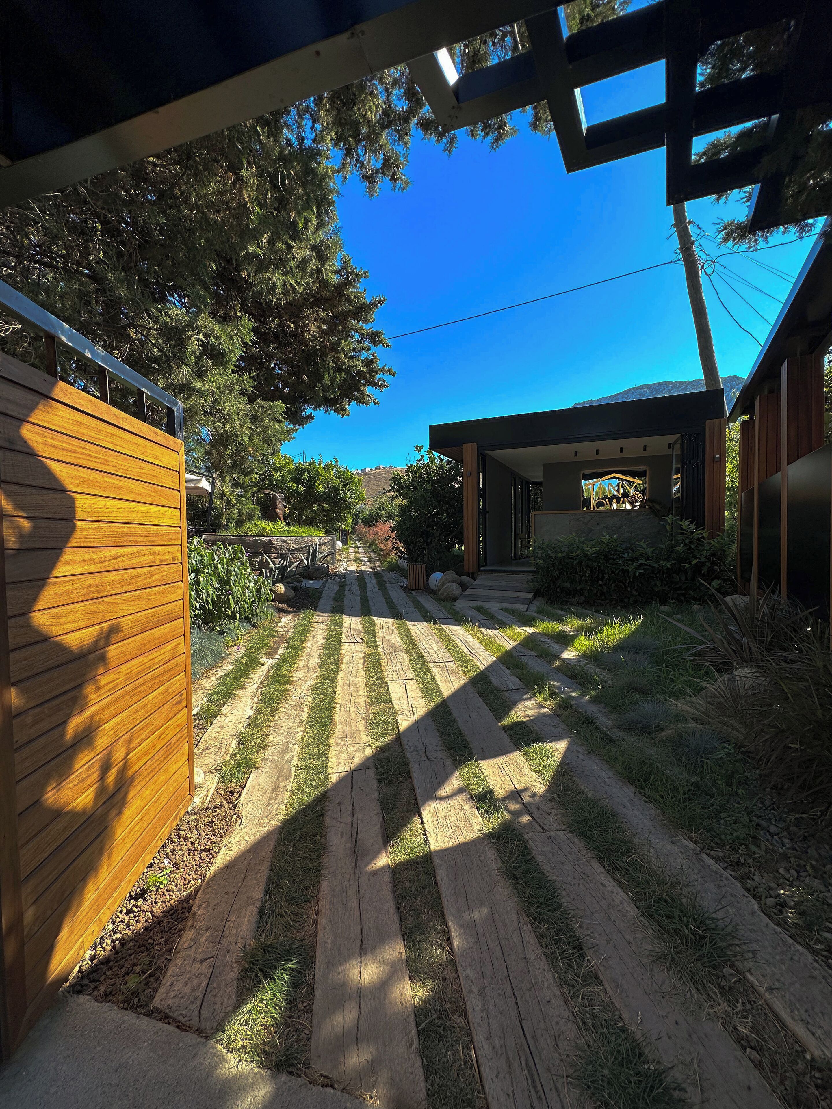 A modern house with a wooden fence, a paved pathway, and a view of a hill.