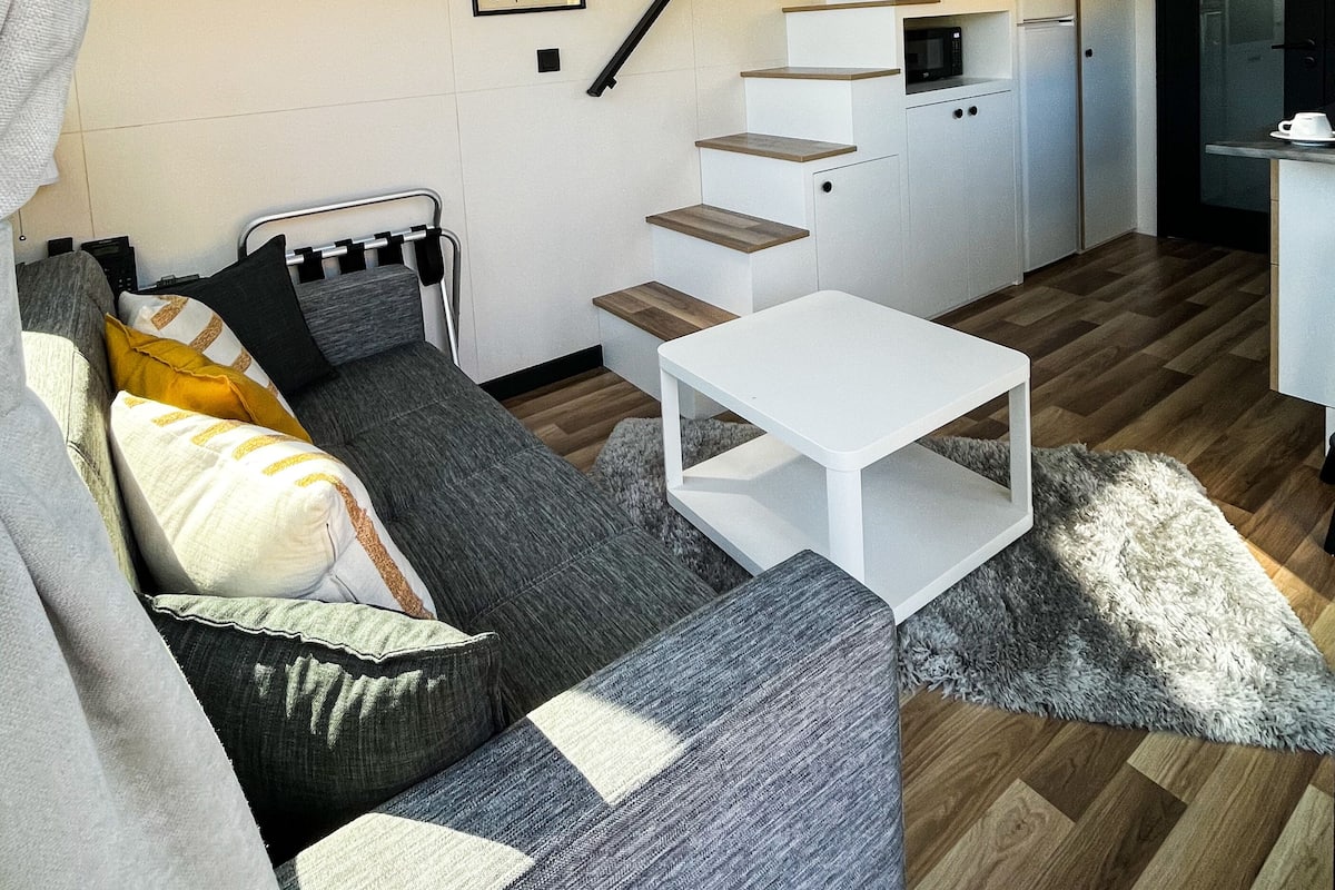 Un espacio de estar moderno con sofá, una mesita de centro, una escalera y una zona de cocina.