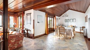 Une pièce spacieuse avec un plafond en bois, un coin repas comprenant une table et des chaises, et un coin salon confortable avec un canapé.