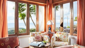Une pièce dotée de grandes fenêtres, d’un canapé, d’une petite table avec une lampe et offrant une vue sur la mer.