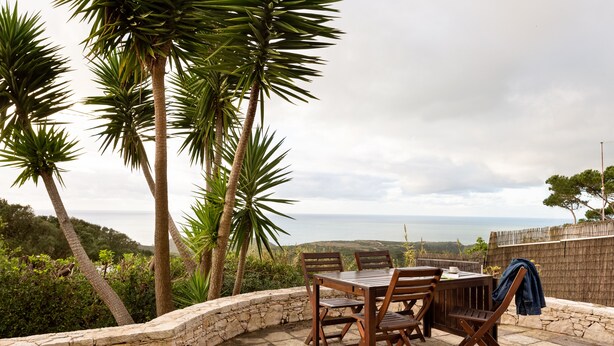 Une terrasse extérieure avec un mur en pierre, une table et des chaises en bois, et une vue sur la mer.