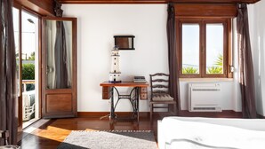 Une pièce avec un plafond en bois, un bureau avec une lampe, une chaise, un radiateur et une grande fenêtre avec des rideaux.