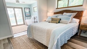 A bedroom with a large bed, a window, a ceiling fan, and a view of a balcony.