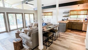 A spacious living area with a large sofa, a dining table, and a kitchen area with wooden cabinets and a window.