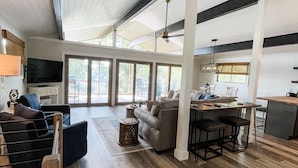 A spacious living area with a high ceiling, wooden flooring, and a large window providing natural light.