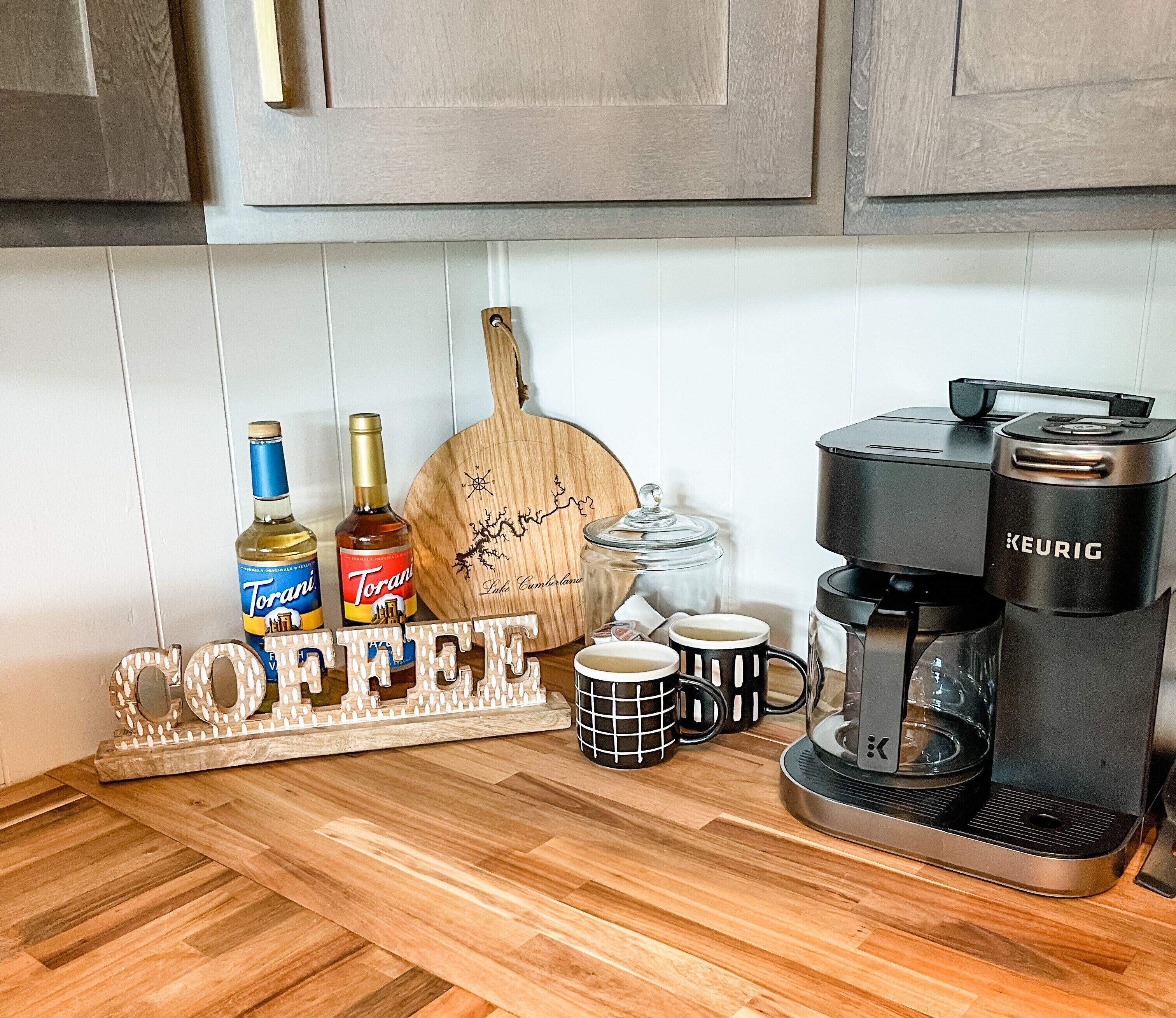 Keittiön työtasolla on kahvinkeitin, kaksi pulloa väkevää alkoholijuomaa, puinen leikkuulauta, puinen kyltti, jossa lukee sanat »COFFEE» ja »FREE», sekä kaksi mukea.