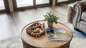 A round wooden coffee table with a woven pattern, a small potted plant, and a magazine on it.