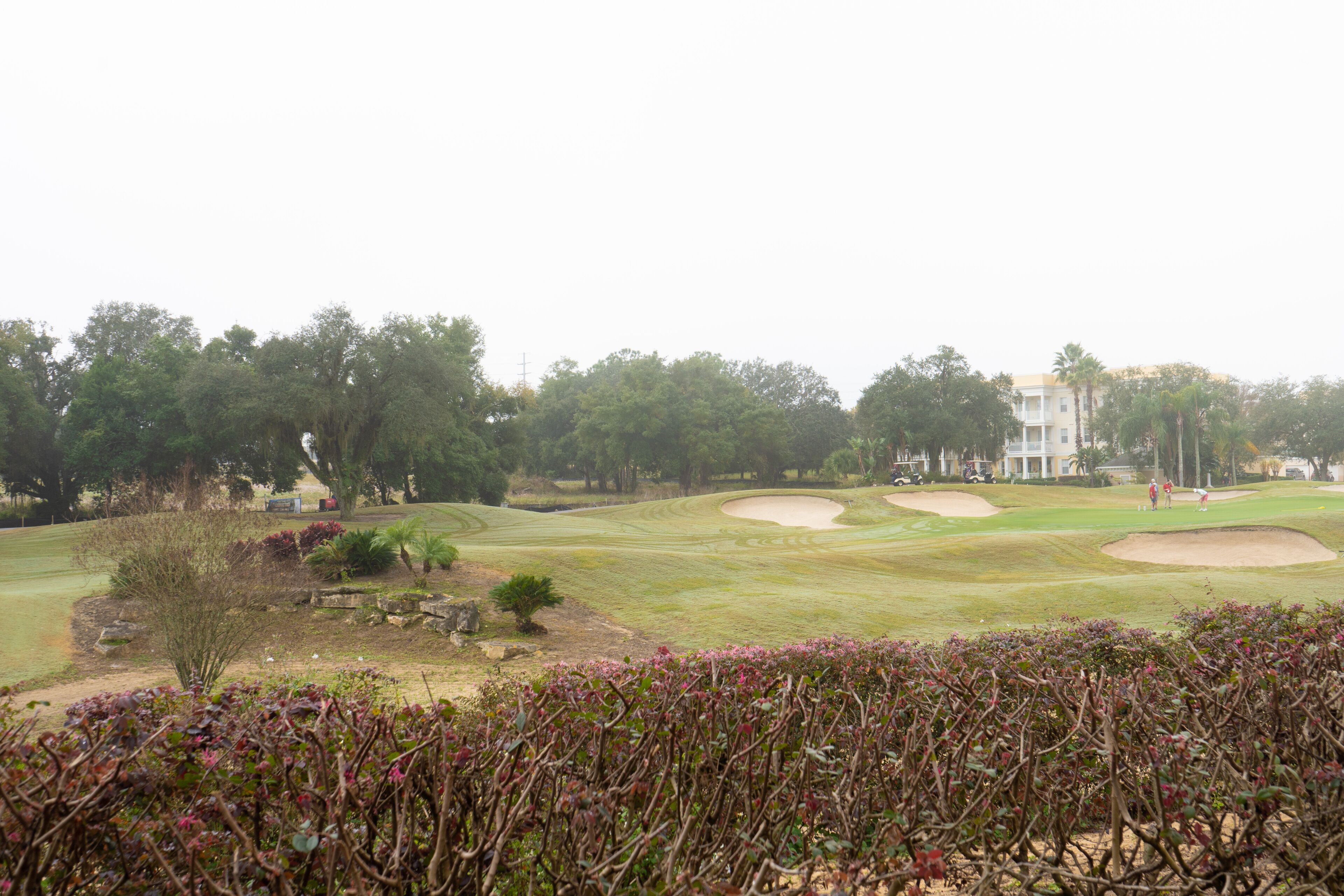 Un parcours de golf avec des bunkers de sable, des arbres et un bâtiment en arrière-plan.