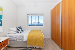 A bedroom with a bed, a window with a view, a wardrobe, and a desk.