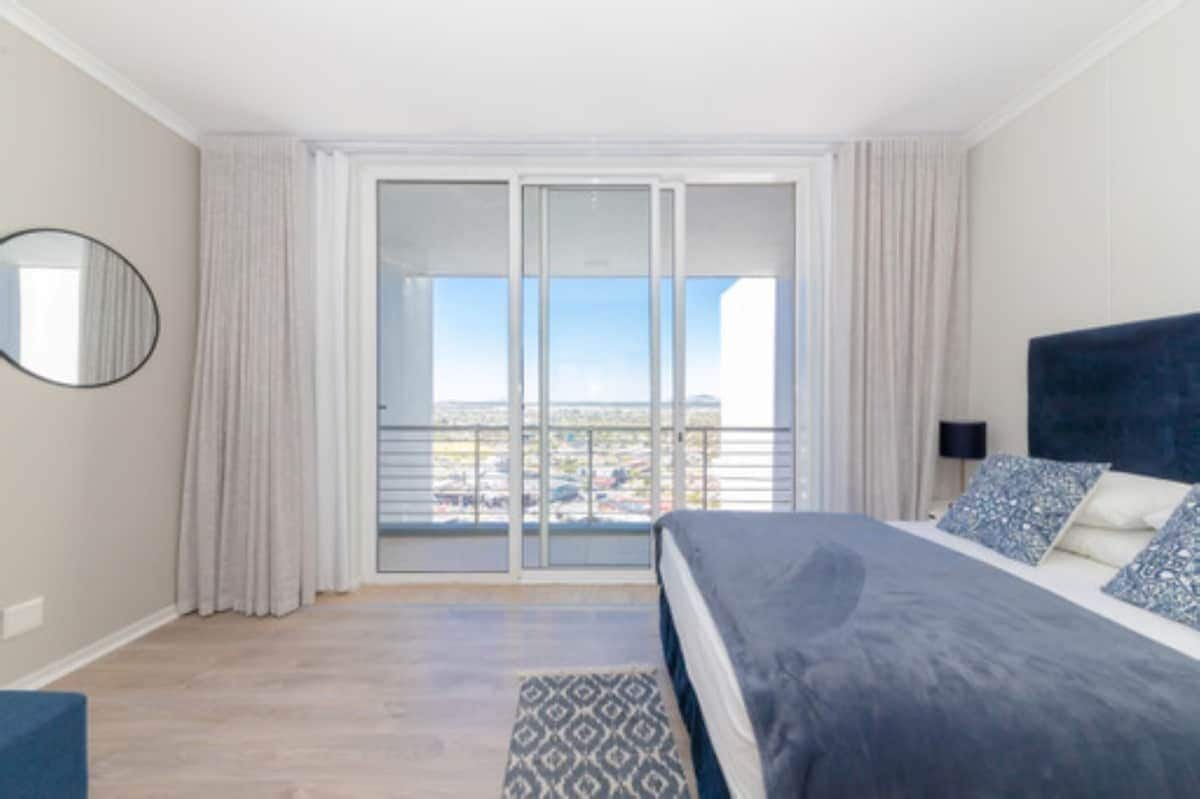 A bedroom with a large bed, a view through a sliding glass door, and a balcony.