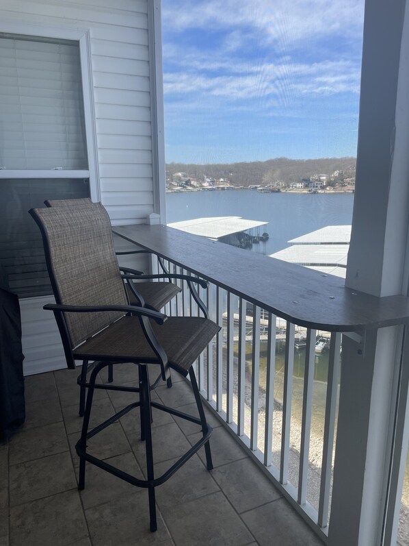 A balcony with a view of a lake and houses, featuring two chairs and a table.