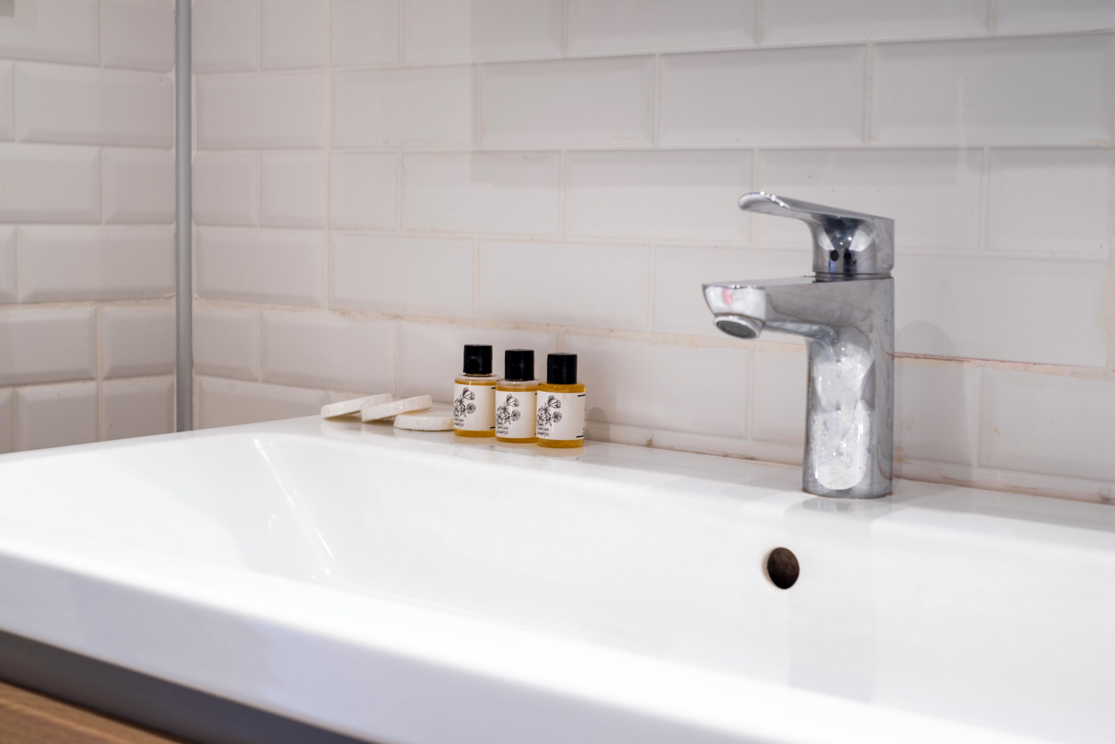 A bathroom with a white sink, a chrome faucet, and three small bottles with labels.