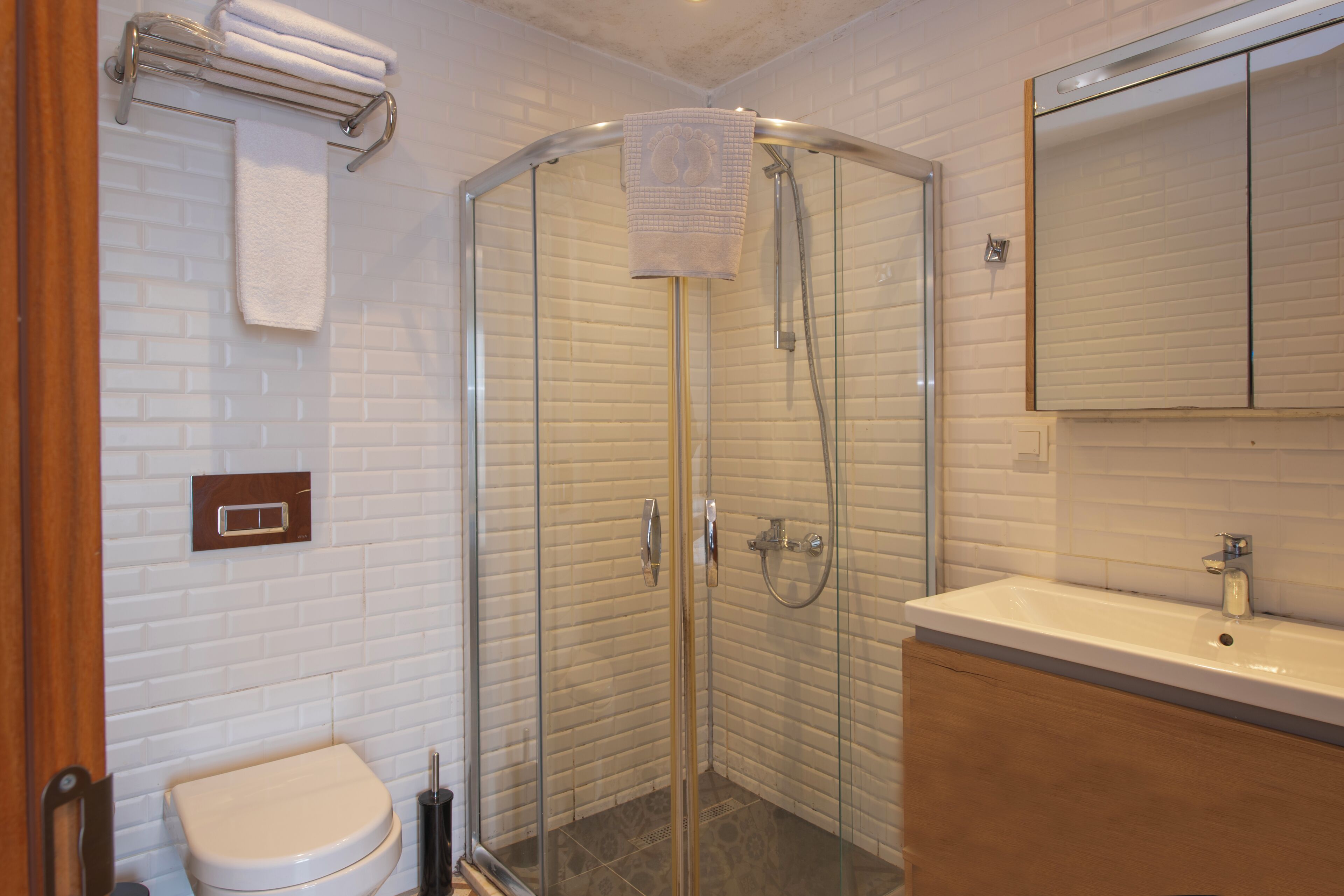 A bathroom with a glass-enclosed shower, a white toilet, a wooden vanity, and a mirror above the sink.