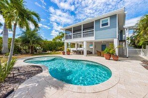 Une maison à deux étages avec une piscine, du mobilier d’extérieur et des palmiers.