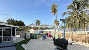 A backyard with a barbecue grill, a potted plant, and a play area with colorful stools.