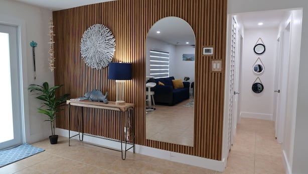 A modern living room with a large mirror, a wooden accent wall, a blue sofa, and a small table with decorative items.