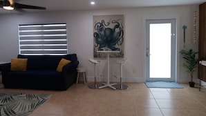 A living room with a dark blue sofa, a small round table, a ceiling fan, and a large abstract painting on the wall.