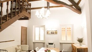 Een rustieke eethoek met een houten tafel, witte stoelen en een trap naar een hoger niveau.