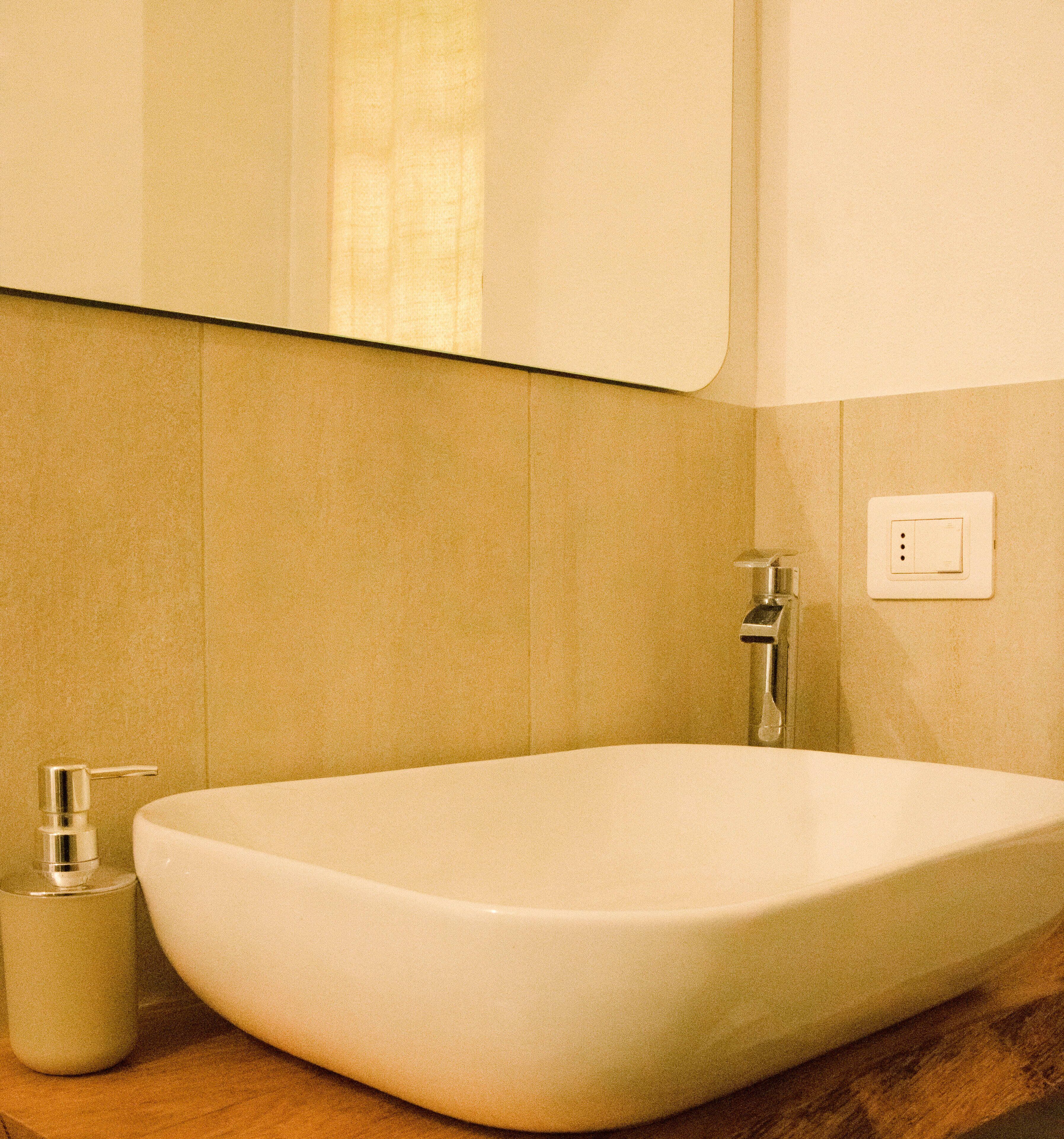 A bathroom with a large white vessel sink, a faucet, and a soap dispenser on a wooden countertop.