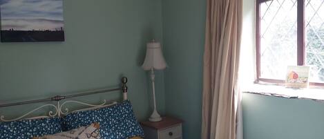 Un dormitorio con cama, mesita de noche, lámpara, ventana con cortinas y lámpara colgante.