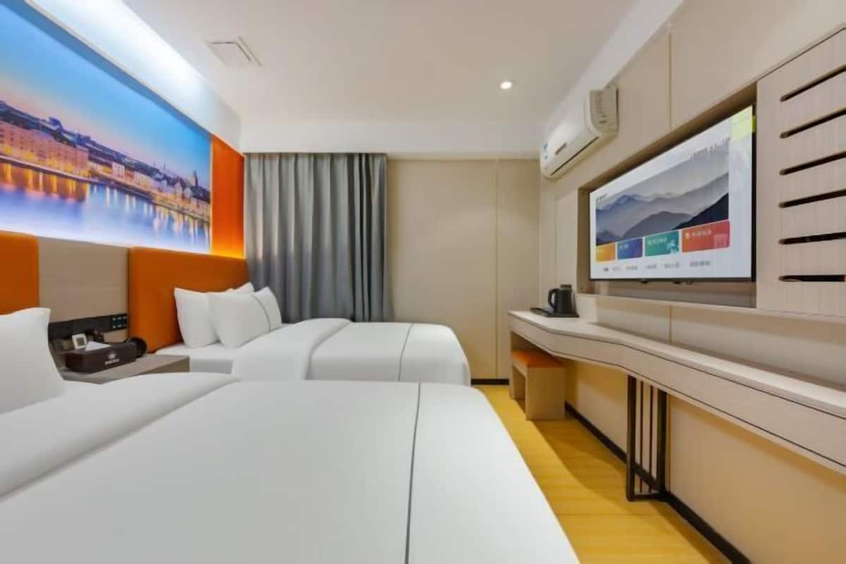 A hotel room with a large bed, a TV mounted on the wall, a desk, and a window with curtains.