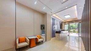 A modern hotel lobby with a reception desk, seating area with orange chairs, and a water dispenser. - YuanRui Hotel ( Financial City Keyun Road Subway Station Store) (Guangzhou)