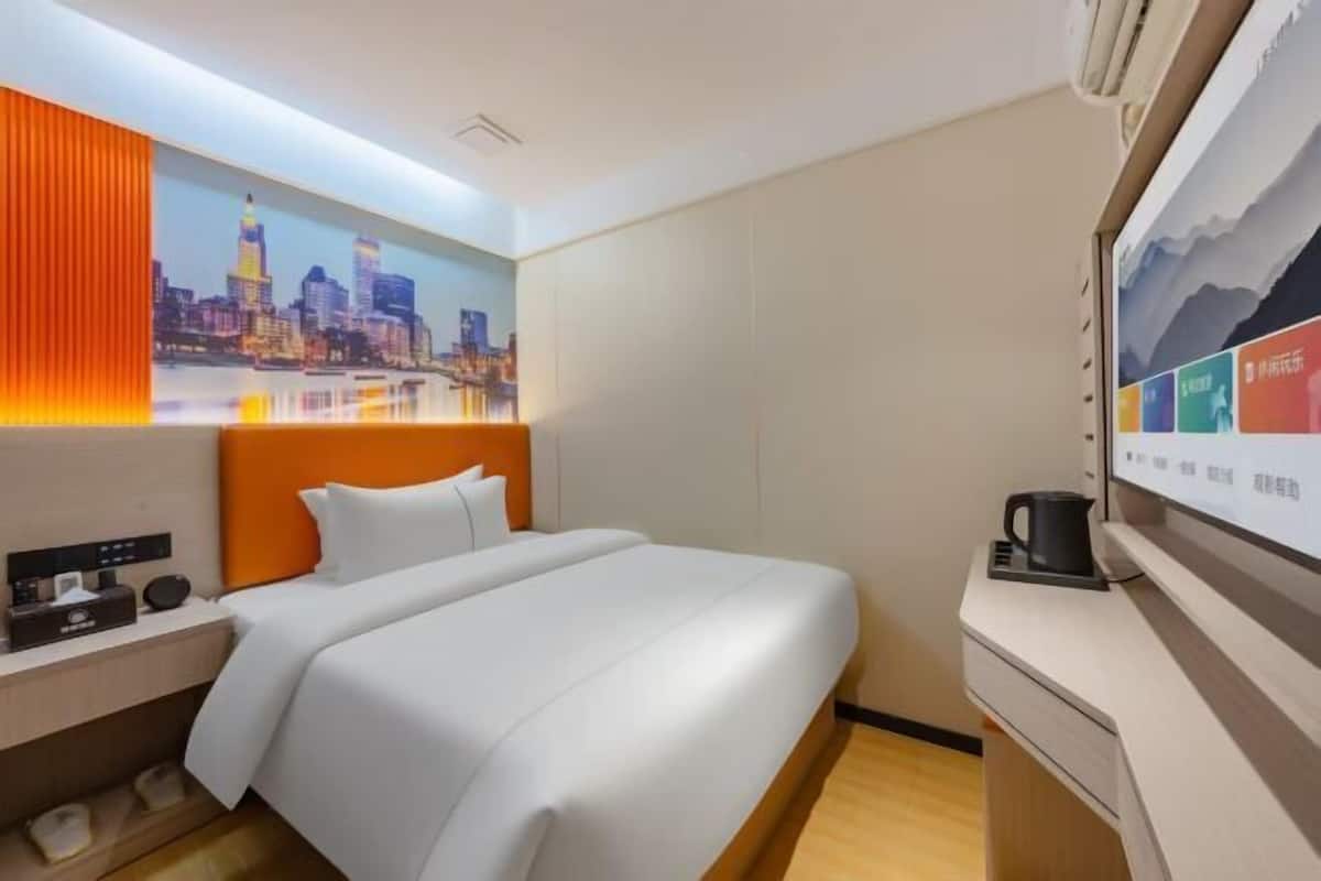A hotel room with a bed, a nightstand, a coffee machine, and a wall with a cityscape painting.