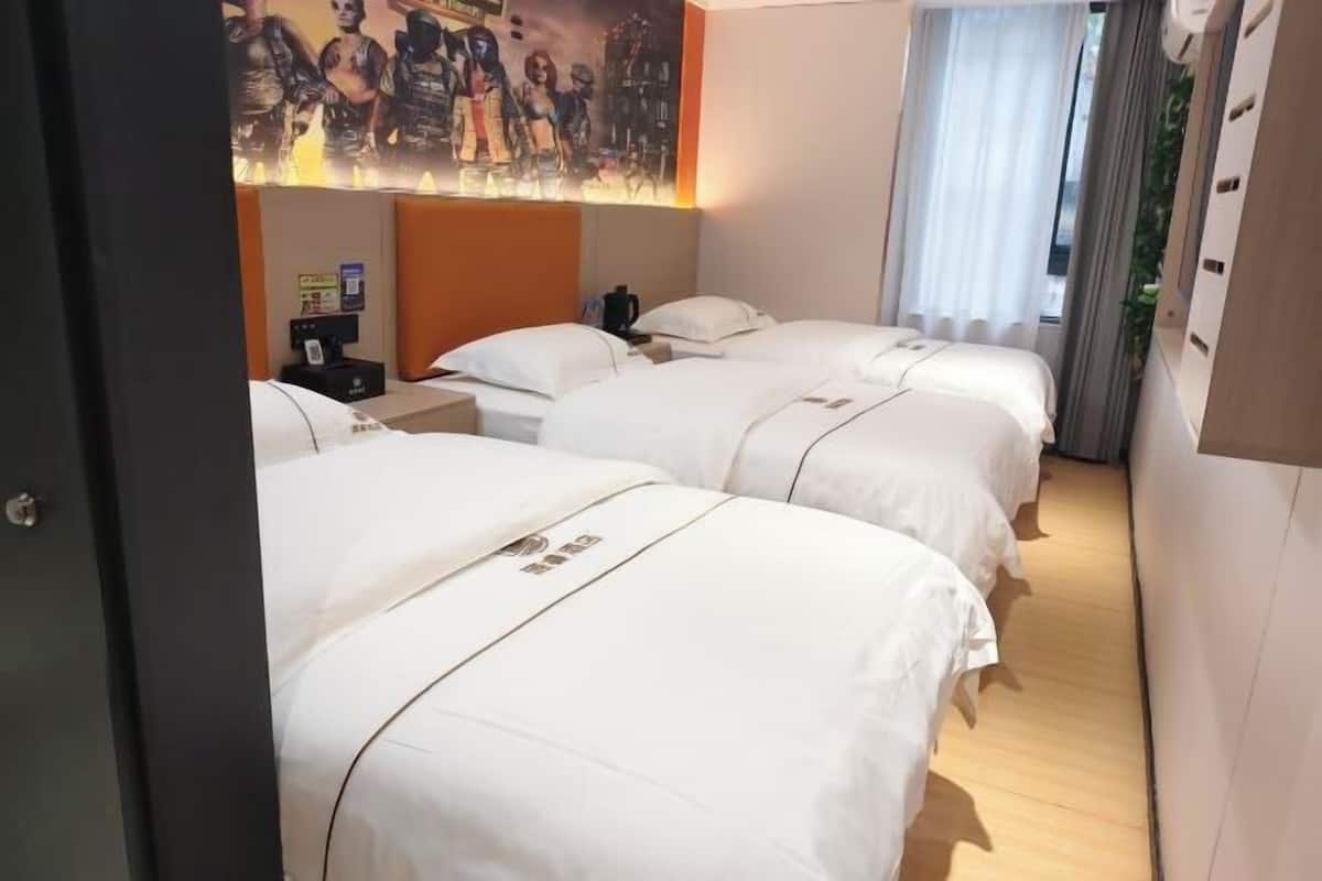 A hotel room with three beds, a nightstand, a wall-mounted TV, and a window with curtains.