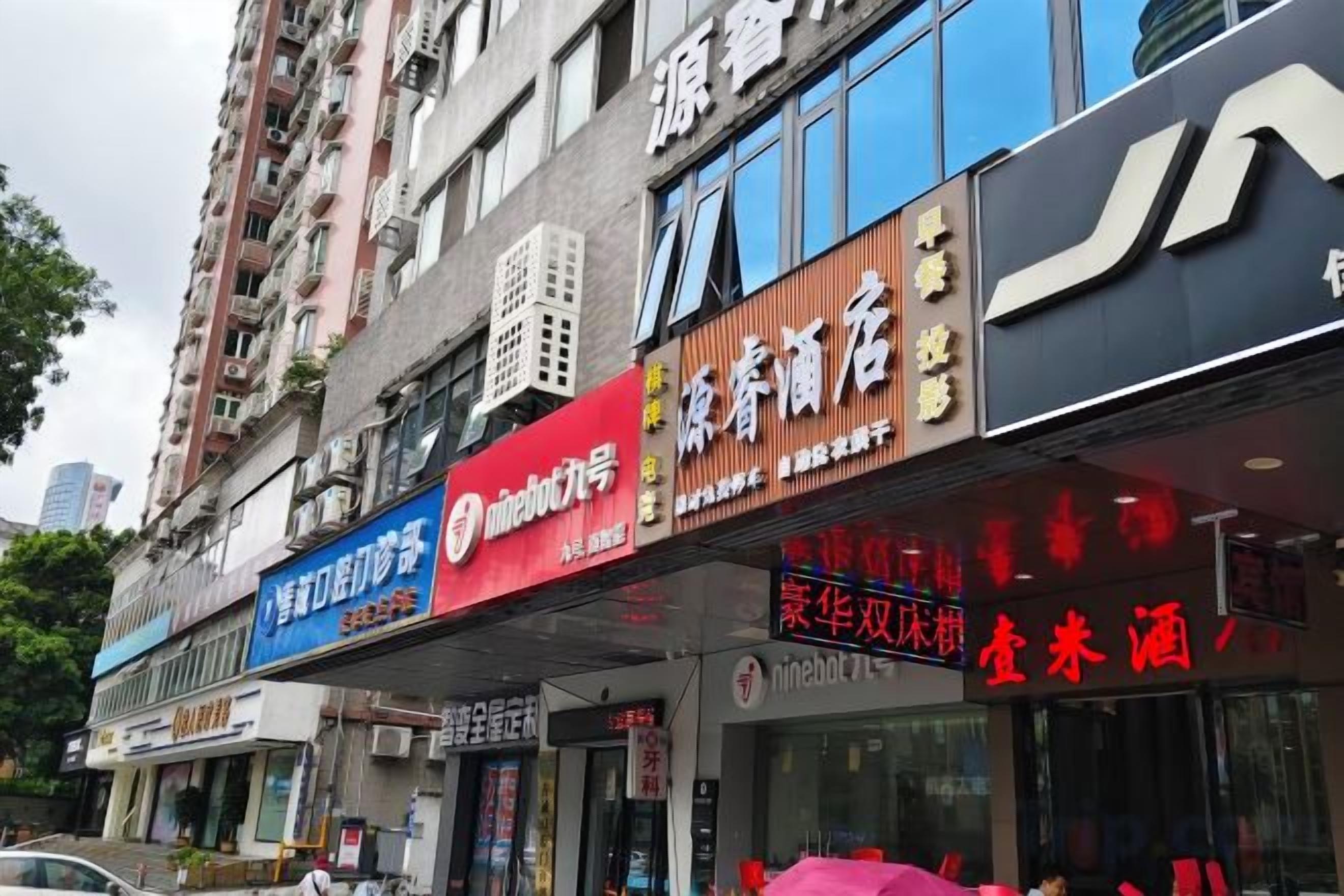 A row of commercial buildings with various storefronts, including a pharmacy and a store with a red sign.