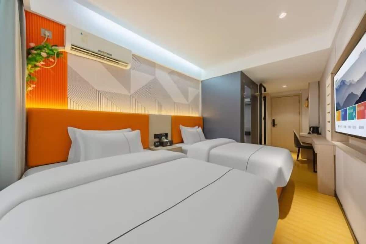 A hotel room with two beds, an orange accent wall, a desk, and a TV.