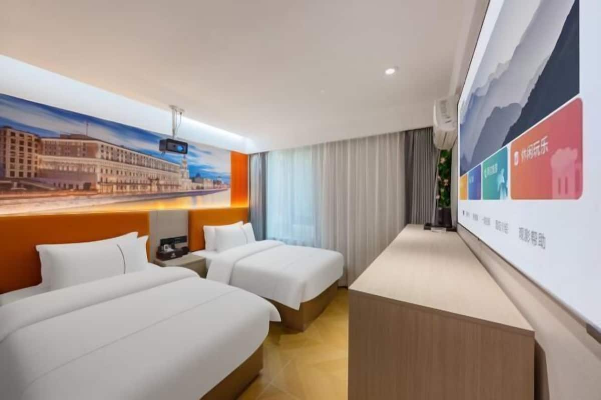 A hotel room with two beds, a desk, a large painting of a cityscape, and a wall with colorful graphics.