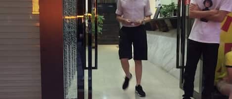 A hotel entrance with glass doors, a reception desk, and a staircase leading to the upper floors.