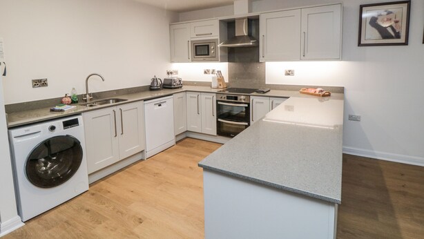 A modern kitchen with white cabinets, a built-in oven, microwave, and dishwasher.