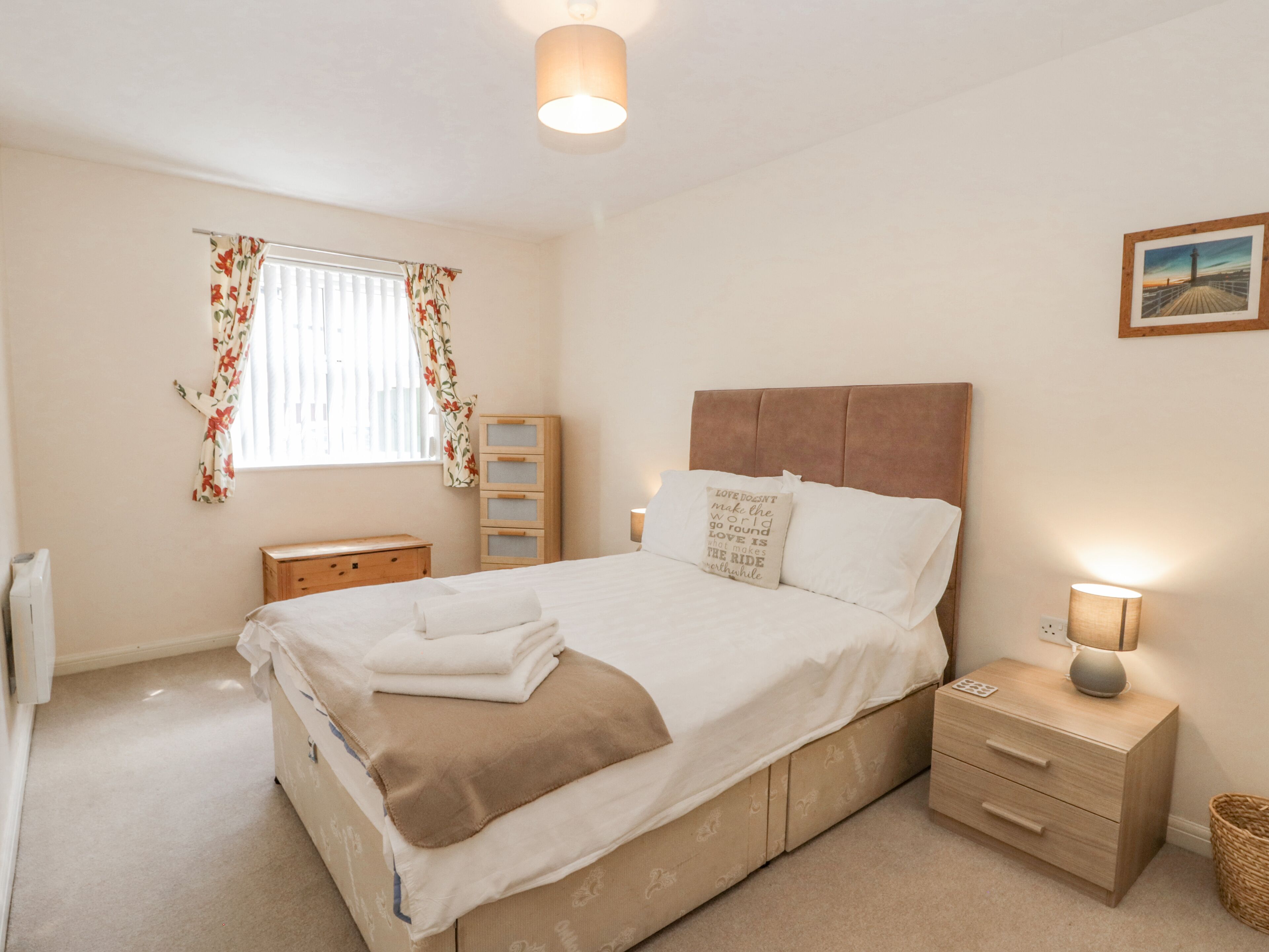 A neatly arranged bedroom with a bed, bedside tables, a nightstand, a lamp, and a window with curtains.