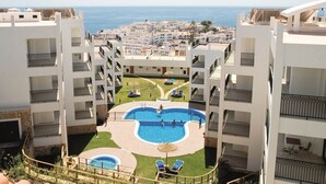 Ein Hotel mit einem zentral gelegenen Pool, umgeben von Balkonen, mit freiem Blick auf das Meer und einer gepflegten Rasenfläche.