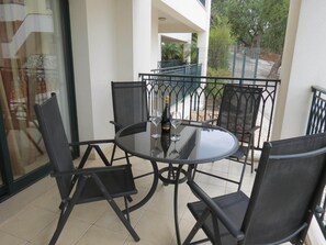 A balcony with a round glass table and four chairs, a bottle of champagne, and a glass on the table.
