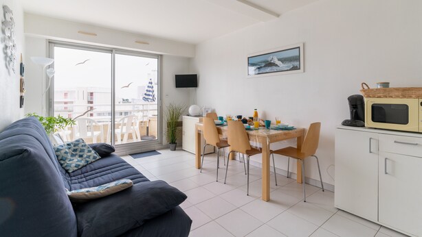 A modern living room with a sofa, dining table, chairs, a TV, and a kitchen area with a microwave. - Océane - Front de mer (Pornichet)