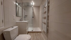 A modern bathroom with a toilet, sink, and glass-enclosed shower. - Océane - Front de mer (Pornichet)