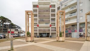 A multi-story building with a central entrance, balconies, and a parking area in front. - Océane - Front de mer (Pornichet)