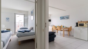 A modern, well-lit room with two beds, a dining area with a table and chairs, and a kitchenette. - Océane - Front de mer (Pornichet)