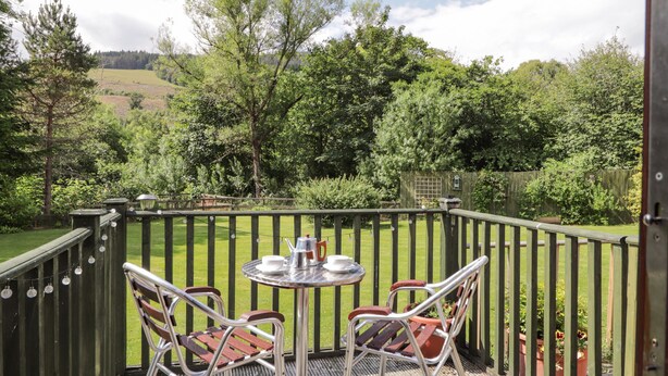 A patio with a round table and two chairs, surrounded by a wooden fence and greenery. - Iola (Inverness)