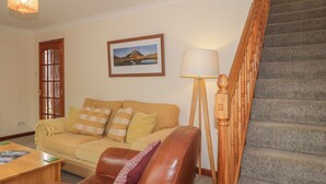 A living room with a sofa, a coffee table, a lamp, and a staircase. - Iola (Inverness)