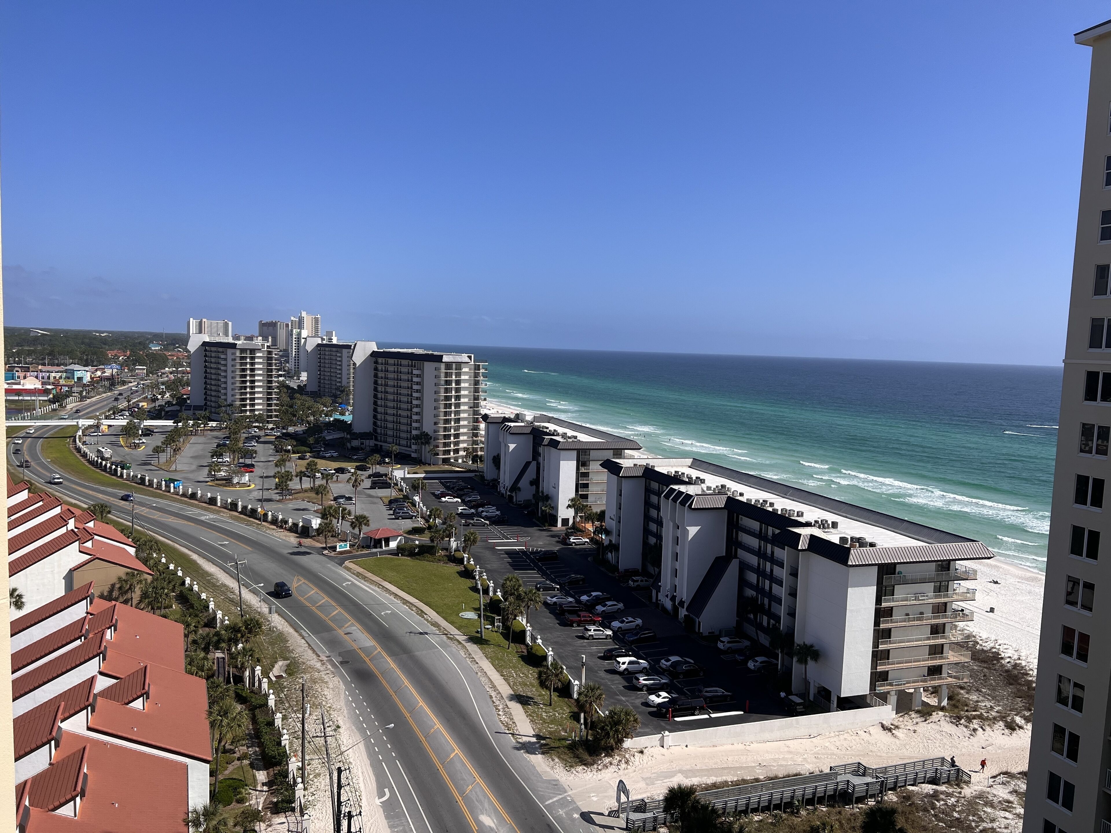 Un paisaje urbano costero con un hotel frente a la playa, una carretera curvada y una vista despejada del océano.